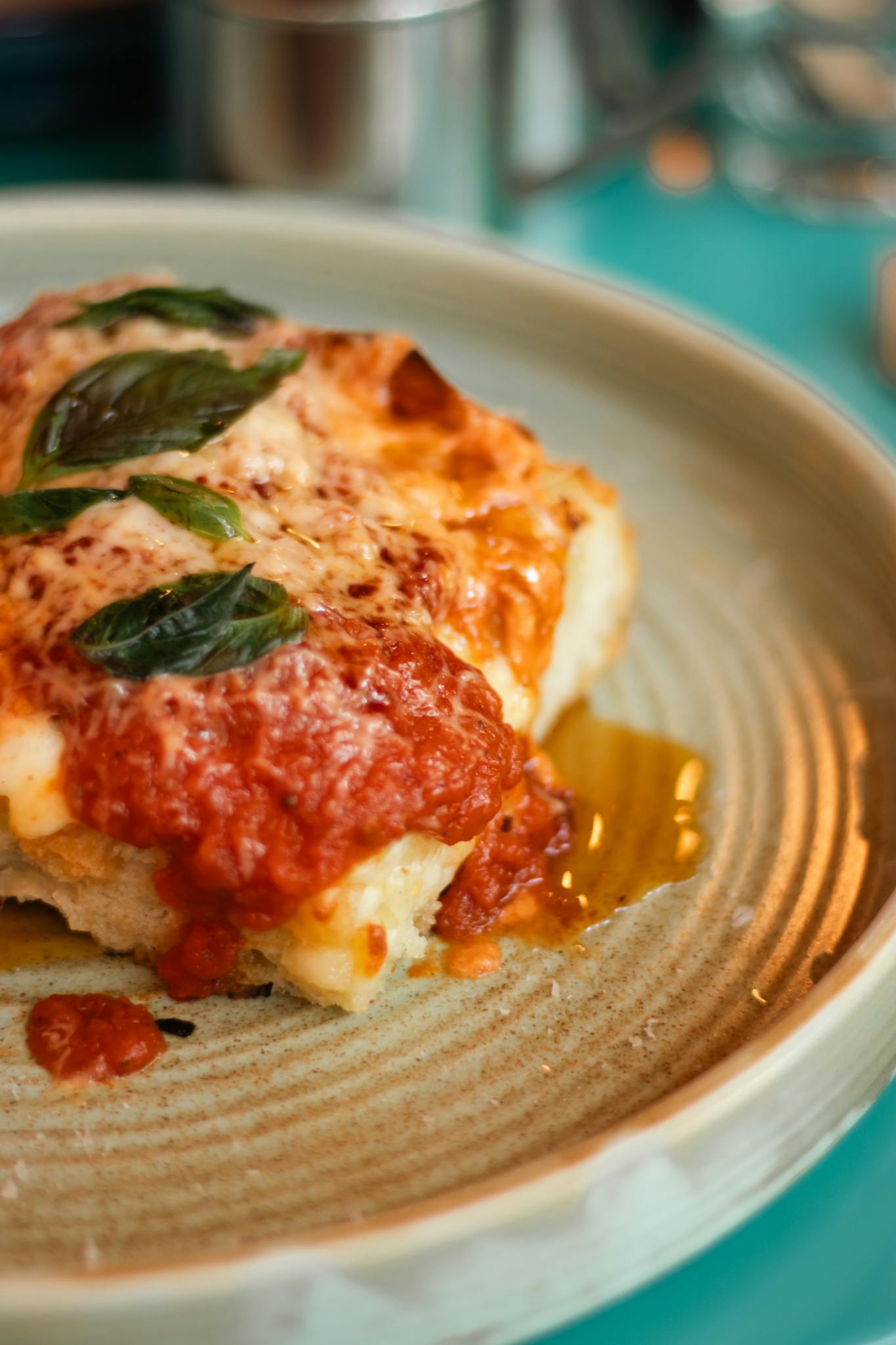 Close-up of homemade lasagna with cheese and basil on a ceramic plate.