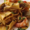 Mezzi paccheri con gamberi in un piatto elegante con pomodorini freschi.