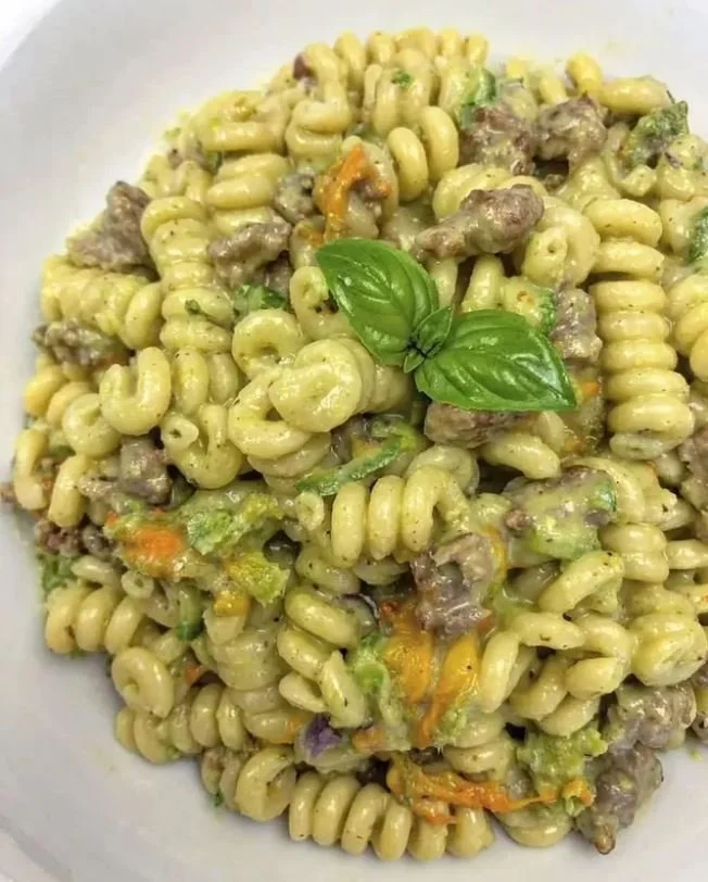 Fussili con fiori di zucchina, zucchine e salsiccia in un piatto gourmet