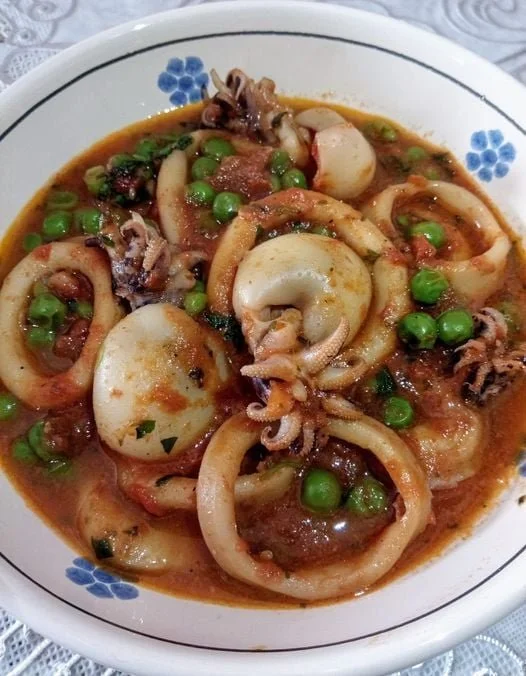 Piatto di calamari e piccoli calamari con piselli e pomodori