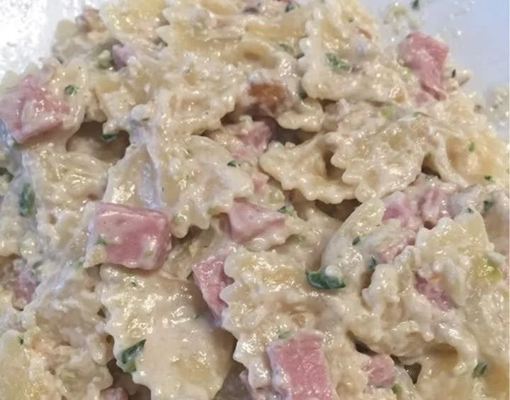 Pasta farfalle con zucchine, prosciutto, Philadelphia e noci in un piatto colorato