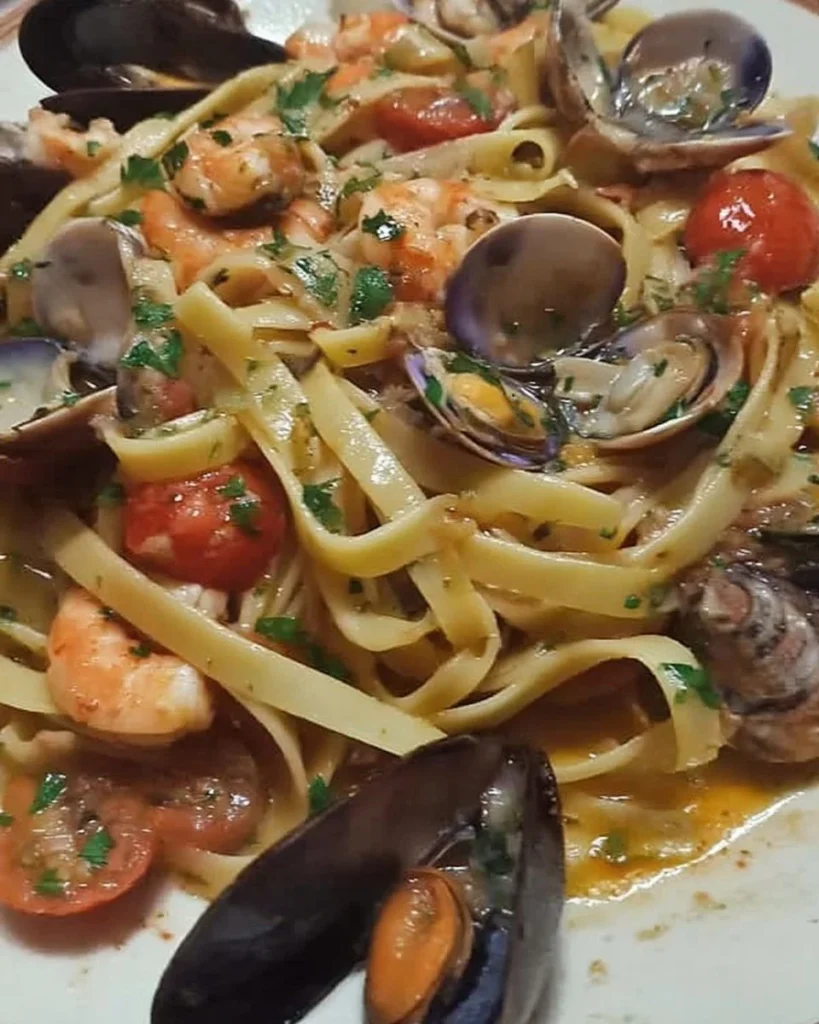 Fettucce con pomodorini, gamberoni, cozze e vongole in un piatto appetitoso