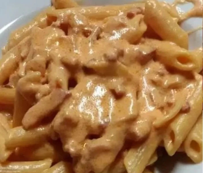 Piatto di penne affumicate servito con salsa cremosa e guarnizioni fresche.