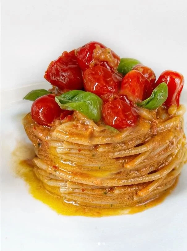 Spaghetti con datterini, burratina e basilico fresco serviti in un piatto colorato.