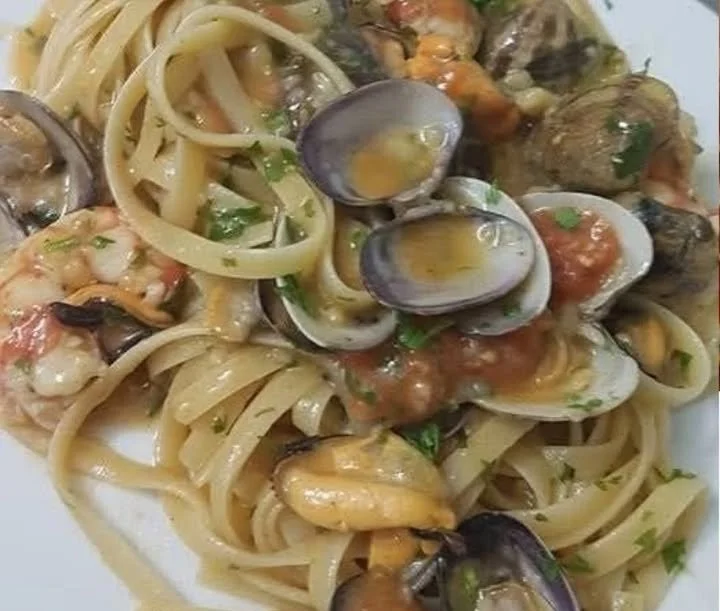 Piatto di Fettucce con pomodorini, gamberoni, cozze e vongole con decorazioni fresche.
