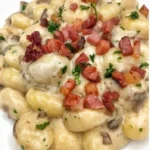 Gnocchi con crema di Parmigiano, funghi e speck serviti in un piatto.