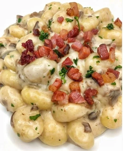 Gnocchi con crema di Parmigiano, funghi e speck serviti in un piatto.