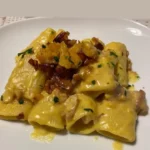 Paccheri con crema di zucca e speck serviti in un piatto elegante.