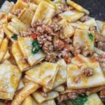 Paccheri con salsiccia, funghi e pomodorini serviti su un piatto