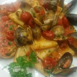 Paccheri con pomodorini freschi e frutti di mare in un piatto colorato.