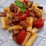 Pasta con melanzane, pomodorini e salsiccia servita in un piatto colorato