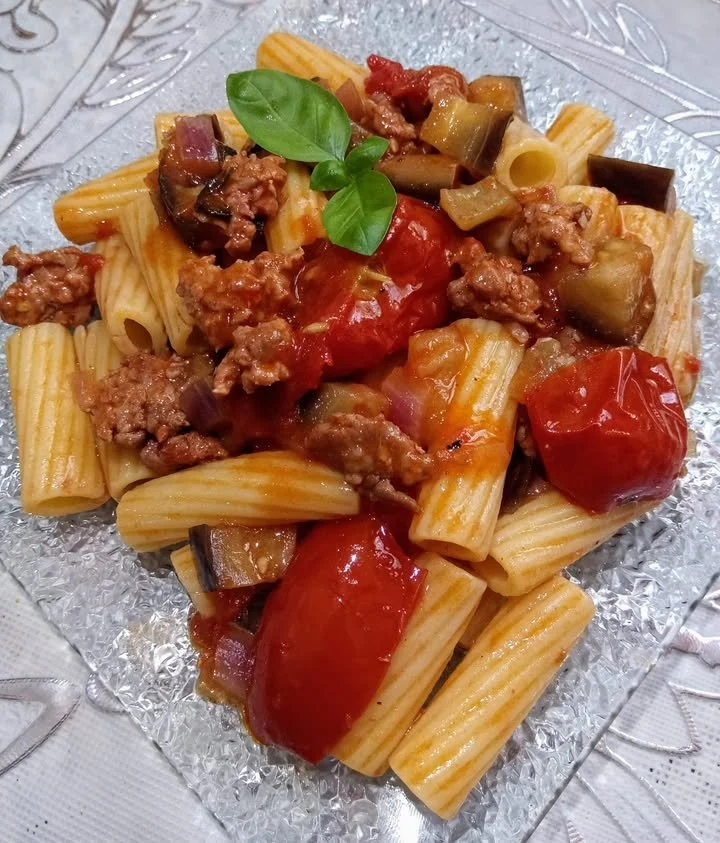 Pasta con melanzane, pomodorini e salsiccia servita in un piatto colorato
