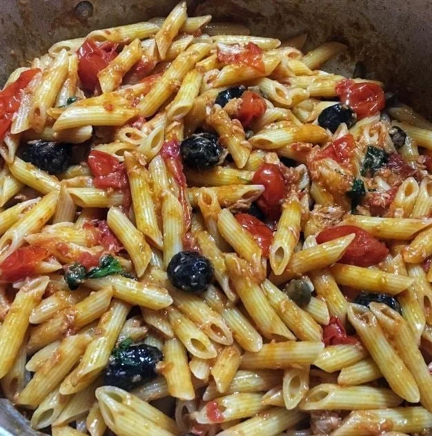 Penne rigate con tonno, pomodorini, olive nere e capperi in un piatto colorato