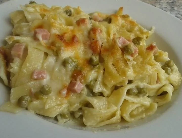 Tagliatelle al forno con prosciutto cotto e piselli serviti su un piatto