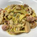 Tagliatelle serviti con funghi porcini e salsiccia in un piatto rustico
