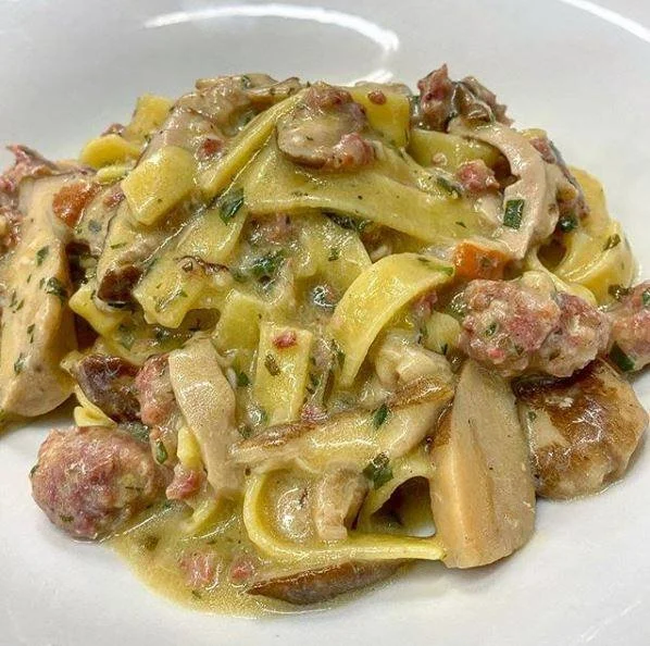Tagliatelle serviti con funghi porcini e salsiccia in un piatto rustico