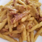 Trofie con crema di pepe, speck e noci su un piatto gourmet.