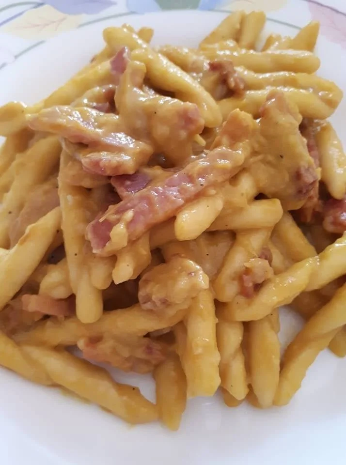 Trofie con crema di pepe, speck e noci su un piatto gourmet.