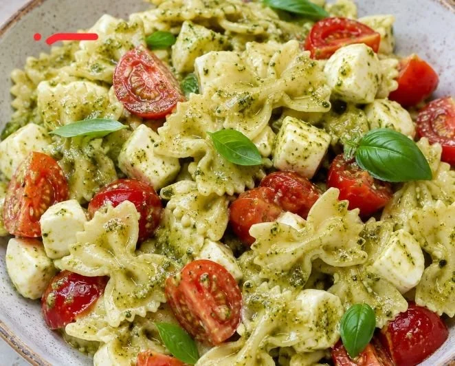 Pasta fredda con mozzarella, pomodorini e pesto servita in un piatto
